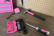 APOLLO TOOLS 13-in-1 Ratcheting Screwdriver with Bit Set – Pink -DT5021P Lifestyle image showing the product near other Apollo tools products. (tape measure, hammer, tool box, scissors)  Shows the pink magnetic ratcheting screwdriver handle and case with bits against wood and peg board background