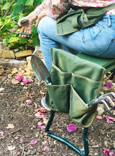 woman wearing green apron sits on garden seat/kneeler in garden and holds pruner