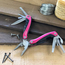 Apollo Tools 14-in-1 Pink High-Quality Pocket Multitool Pliers shown open with all  tools showing against a wood background with rope and wire in back