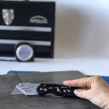 APOLLO TOOLS Ergonomic Black Utility Knife with Carabiner Clip and Fast-Change Blade - DT5017  shown next to vinyl to be cut and Apollo Tools product blurred in the background