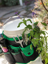 green bucket organizer filled with tools and water flask surrounded by plants